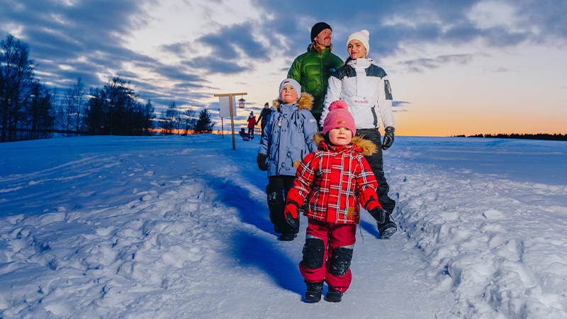 Kaksi aikuista ja kaksi lasta kävelevät talvimaisemassa